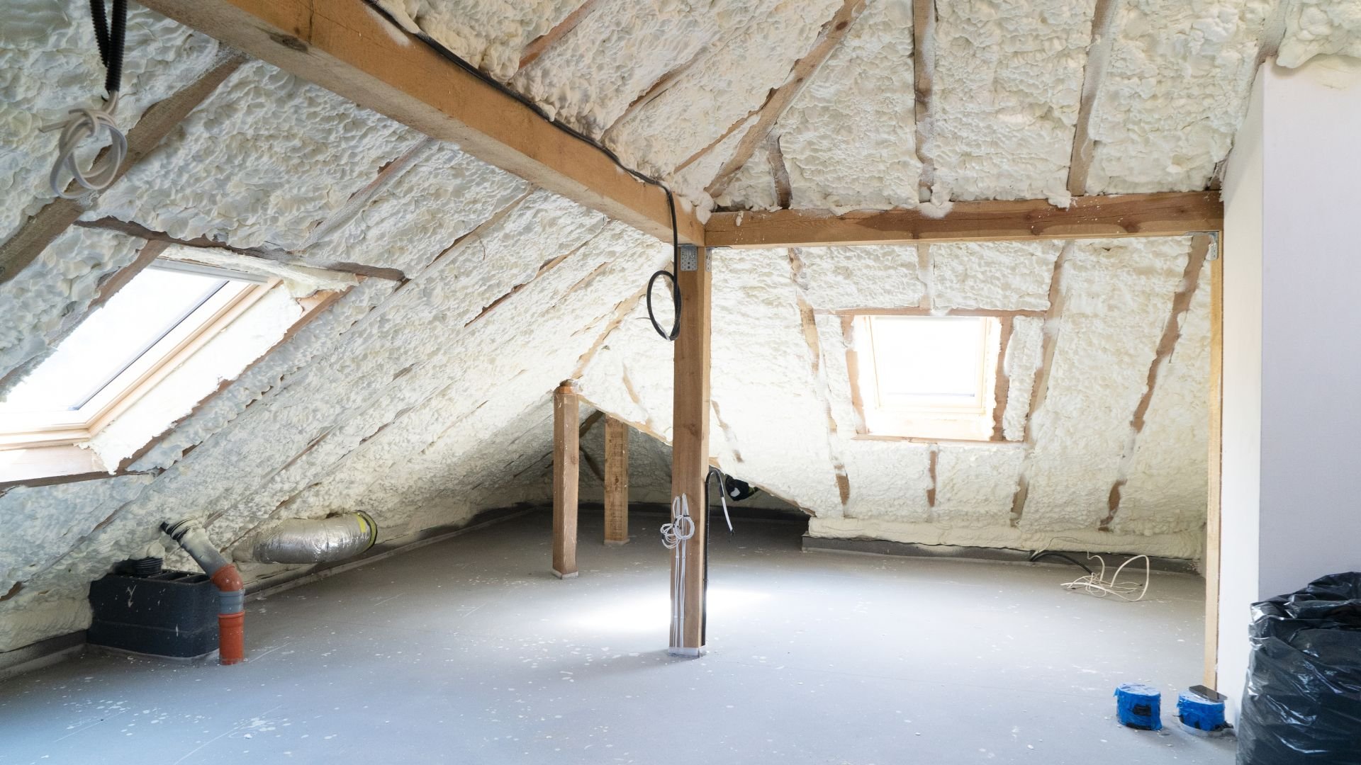 Attic space with spray foam insulation, wooden beams, and skylights